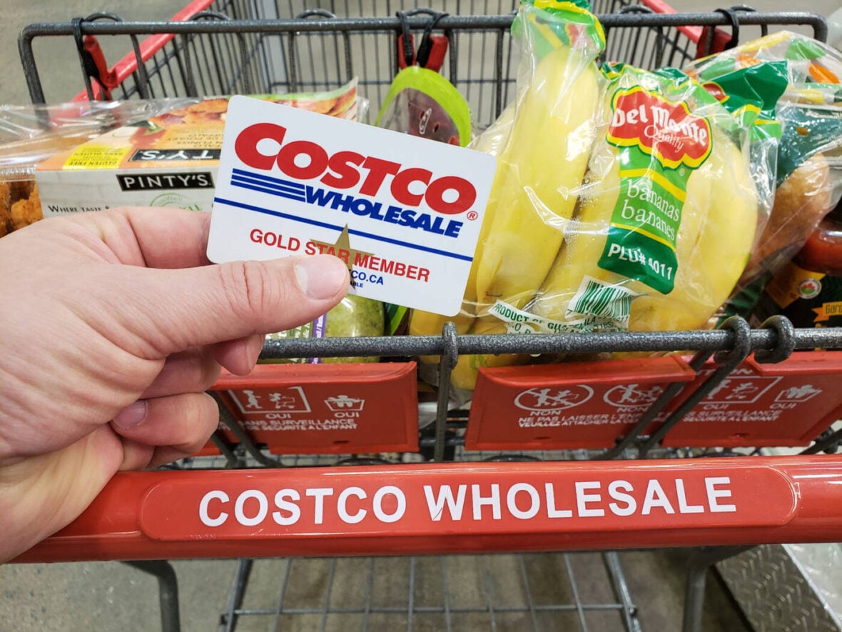 costco benefits A hand holding a Costco Membership card on a cart in Costco warehouse.
